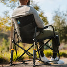 A person relaxing outdoors in a black Freestyle Rocker Elite chair with a mesh back, cup holder, and sturdy frame.