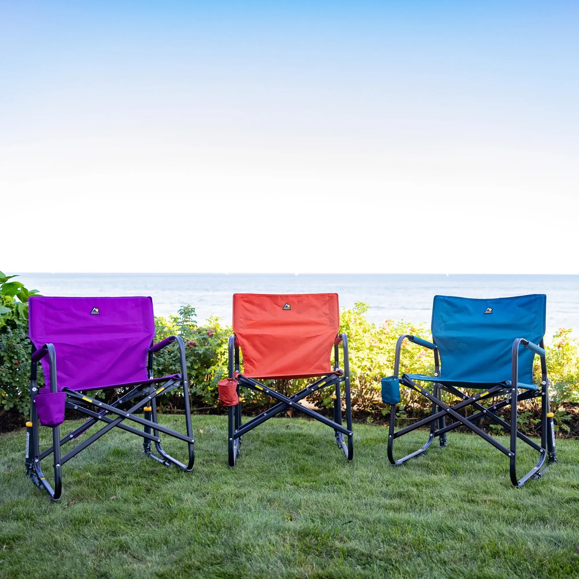 Freestyle rockers in three different colors on grass by the ocean.