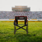 A Freestyle Rocker XL NASCAR chair sitting on a patch of grass in front of a racecar track. 
