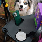 Close-up of the Side Table on a berry Freestyle Rocker XL, holding a phone in the slot and a mug in the cupholder, with a dog in the background.