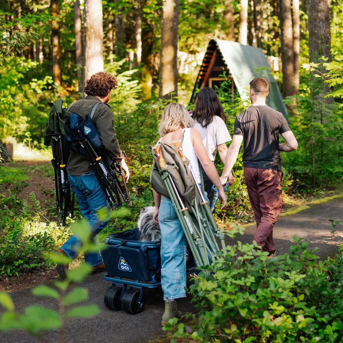 An indigo Go-Hauler wagon loaded with gear is pulled along a wooded path by a group of campers.