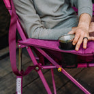 Close-up of a hand resting on the armrest of a berry Kickback Insulated Rocker, with a metal cup set in the built-in cup holder.