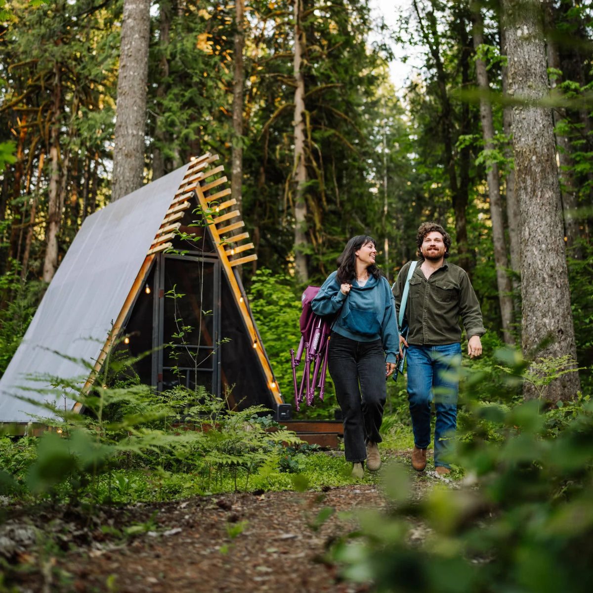 Man and woman walk through the woods carrying a folded berry and a folded teal Kickback Insulated Rocker.