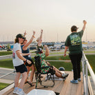 Group of NASCAR fans cheering from a trackside deck at sunset during a race.