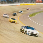 NASCAR race cars speeding through a curved track during a race.