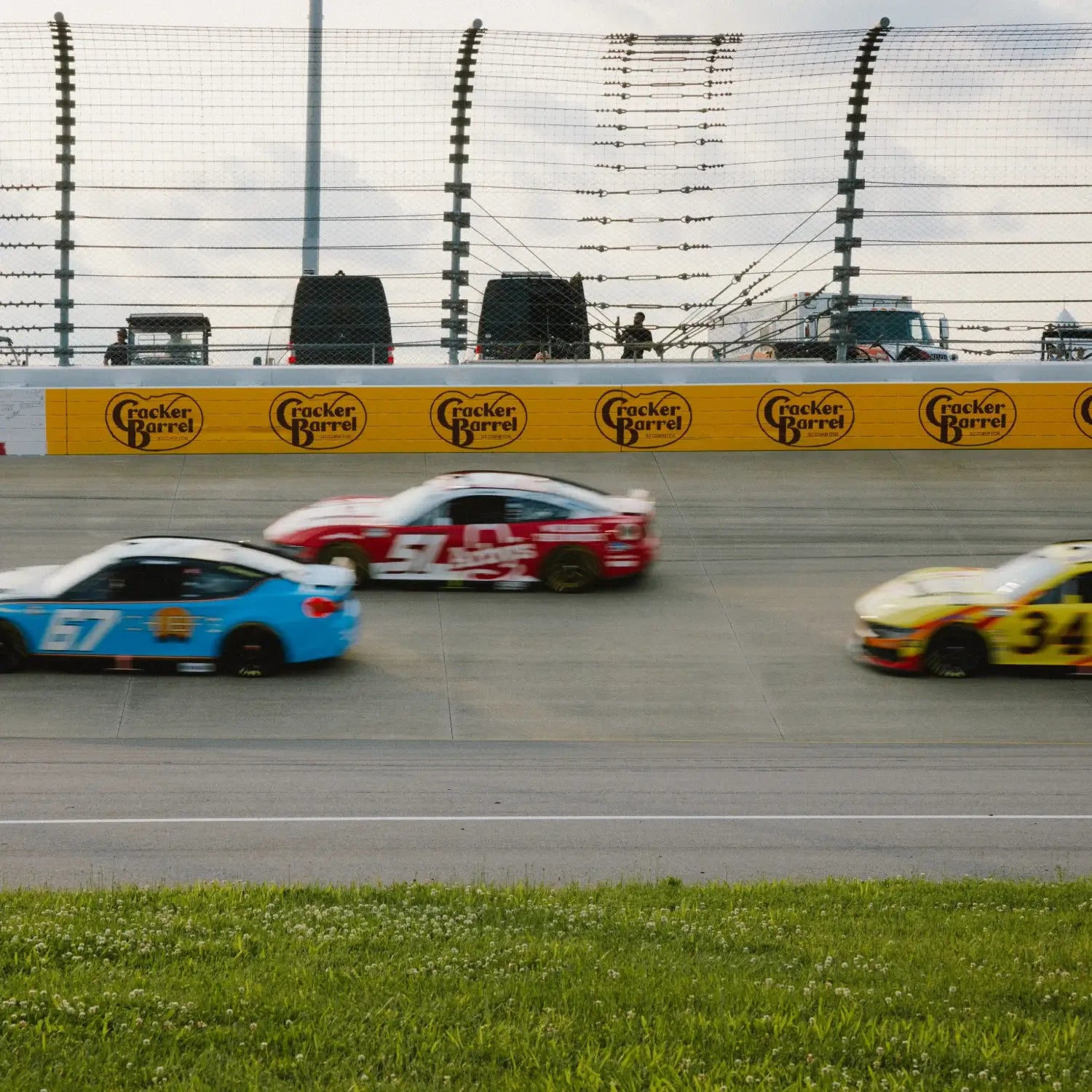 Three NASCAR stock cars racing side by side on a speedway during a daytime race.