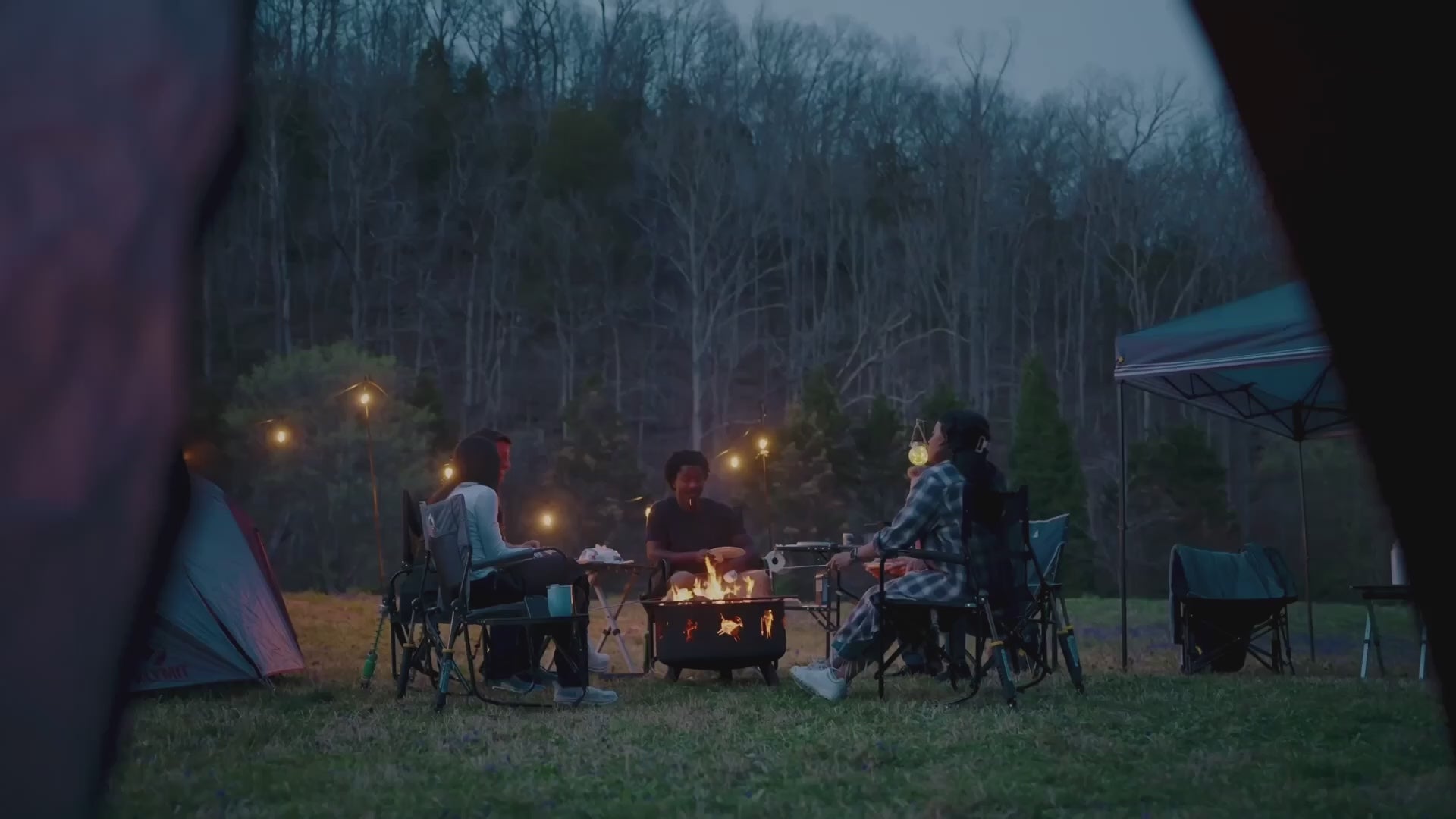 A group of people sitting in gci outdoor chairs around a bonfire. 