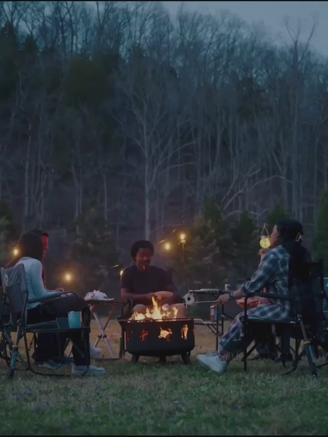 A group of people sitting in gci outdoor chairs around a bonfire. 