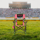 A Roadtrip Rocker NASCAR chair sitting on a patch of grass in front of a racecar track. 