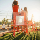 Two women cheering at a softball game beside GCI Outdoor Stowaway Rockers in Coral Mosaic, rear view.