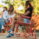 Two women socializing outdoors in GCI Outdoor Stowaway Rockers in Coral Mosaic, with drinks at a backyard gathering.