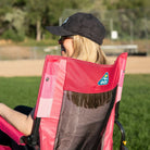 Close-up back view of a woman wearing a cap, seated in a pink flame waves Stowaway Rocker, with GCI logo visible on the chair back.