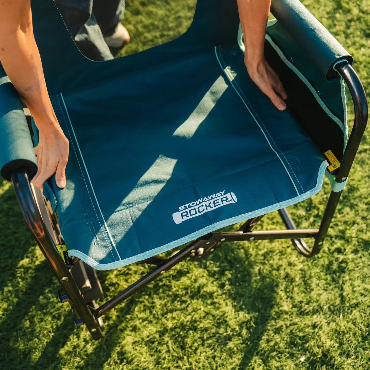 A person unfolding a teal Stowaway Rocker with Side Table. 