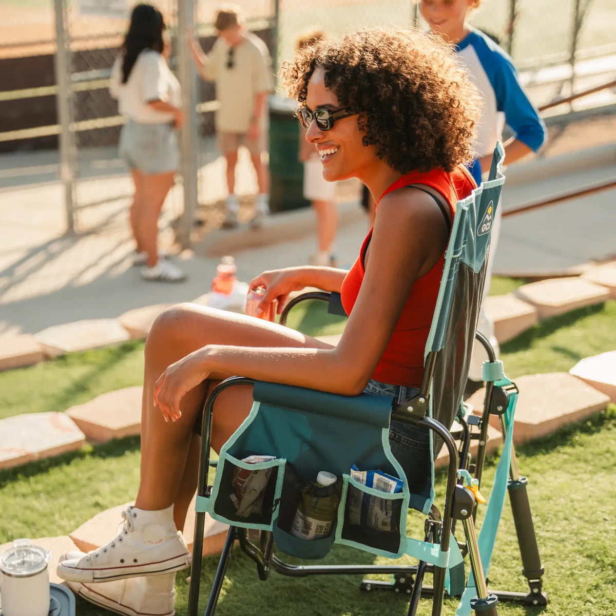 A woman sitting in a teal Stowaway Rocker with Side Table next to a child in a baseball uniform. 
