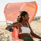 A woman relaxing on a Grab and Go Rocker with a coral Sunshade Accessory attached. 