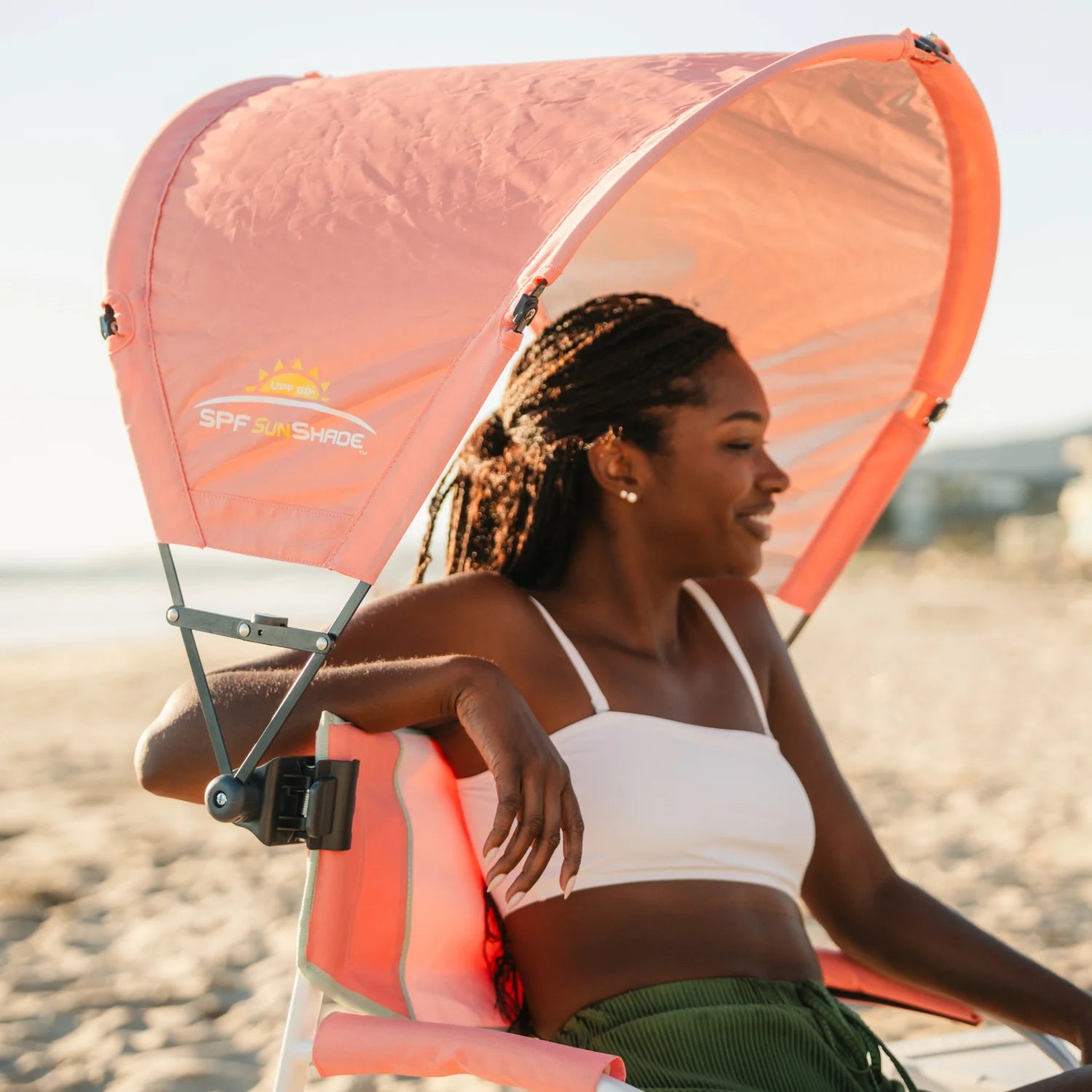 A woman relaxing on a Grab and Go Rocker with a coral Sunshade Accessory attached. 