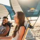 Side profile of a woman at the beach shaded by a teal GCI Outdoor SPF SunShade Accessory during golden hour.