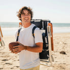 Man carrying TidalDrift indigo stripe backpack beach chair with padded shoulder straps on the beach.