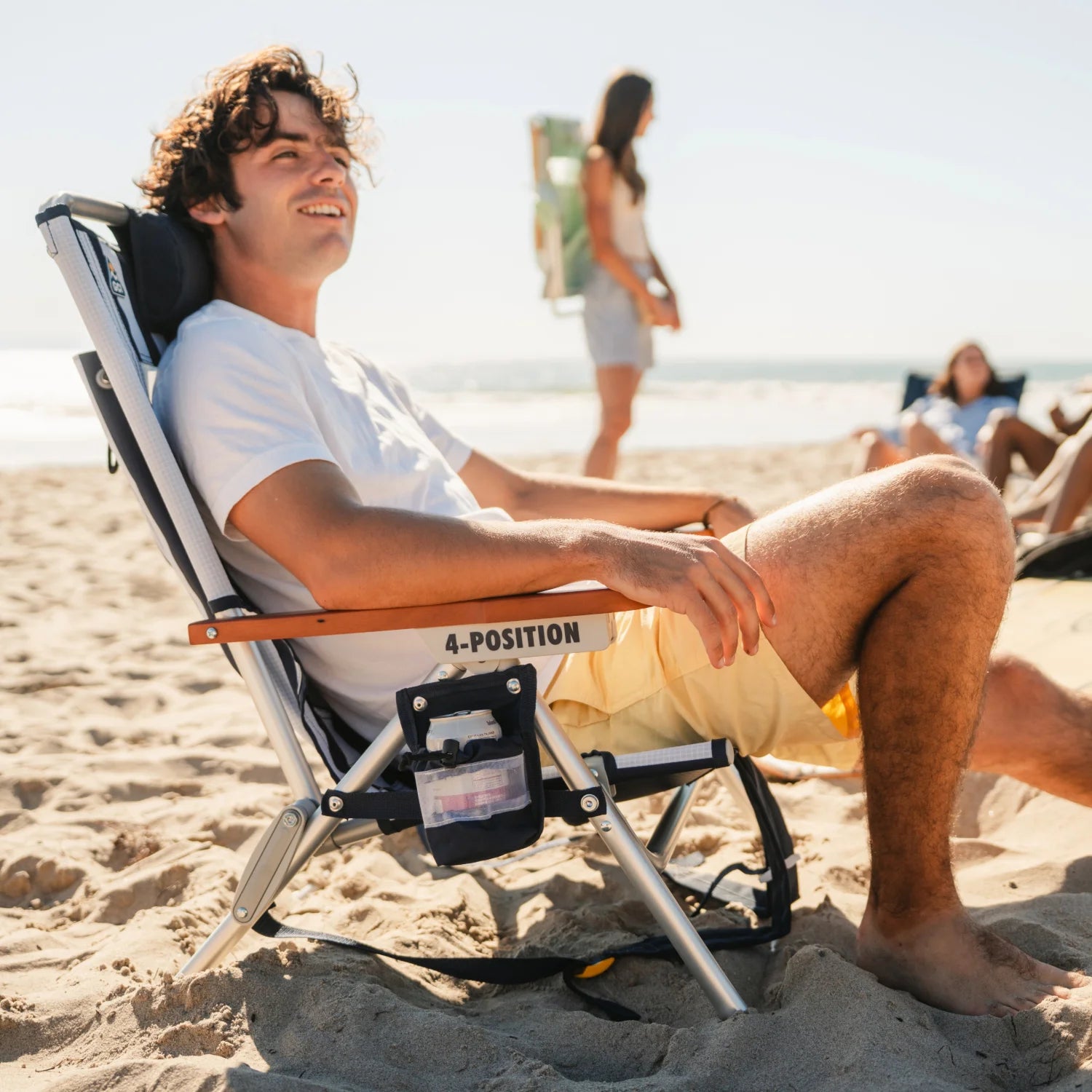 Man reclining in TidalDrift indigo stripe beach chair with drink holder pouch and wood armrest.