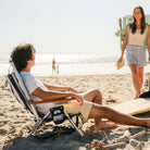 Man relaxing in TidalDrift 4-position backpack beach chair with headrest on the shore.