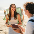 Woman laughing while carrying the TidalDrift pastel green mosaic backpack beach chair on the beach.
